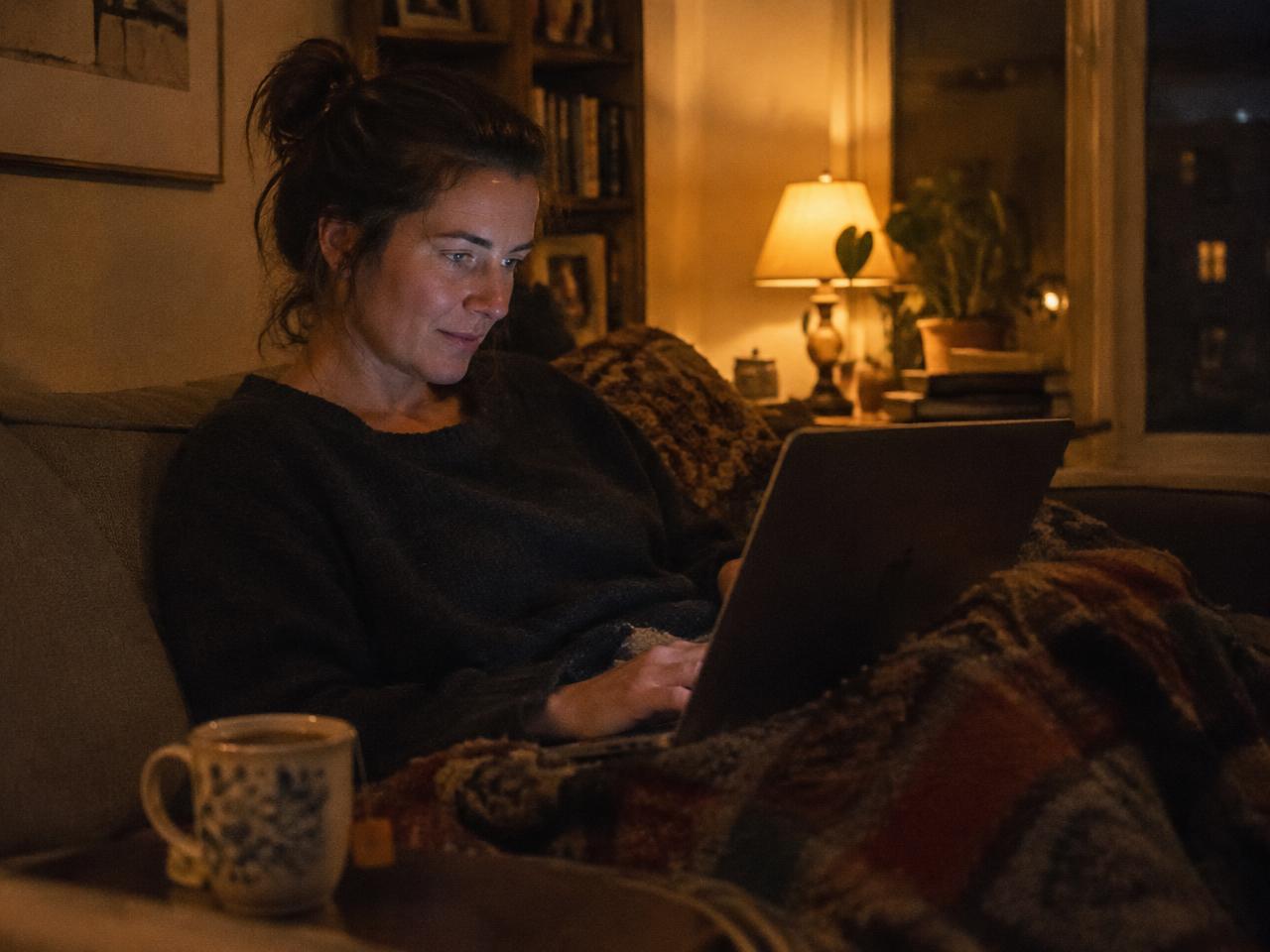 A woman writing on her laptop at home in warm lamplight